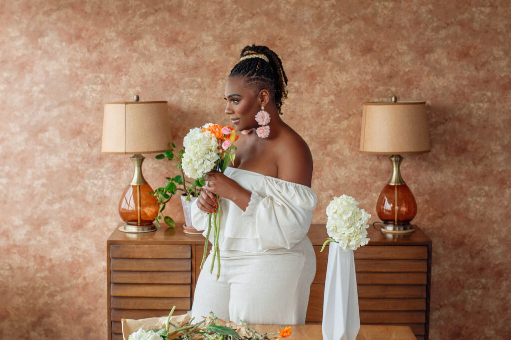 Black woman in a white jumpsuit smelling fresh flowers